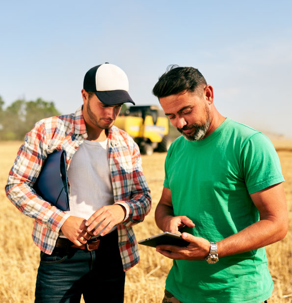 Two men are standing in a harvested wheat field under a clear sky, engaged in a discussion.